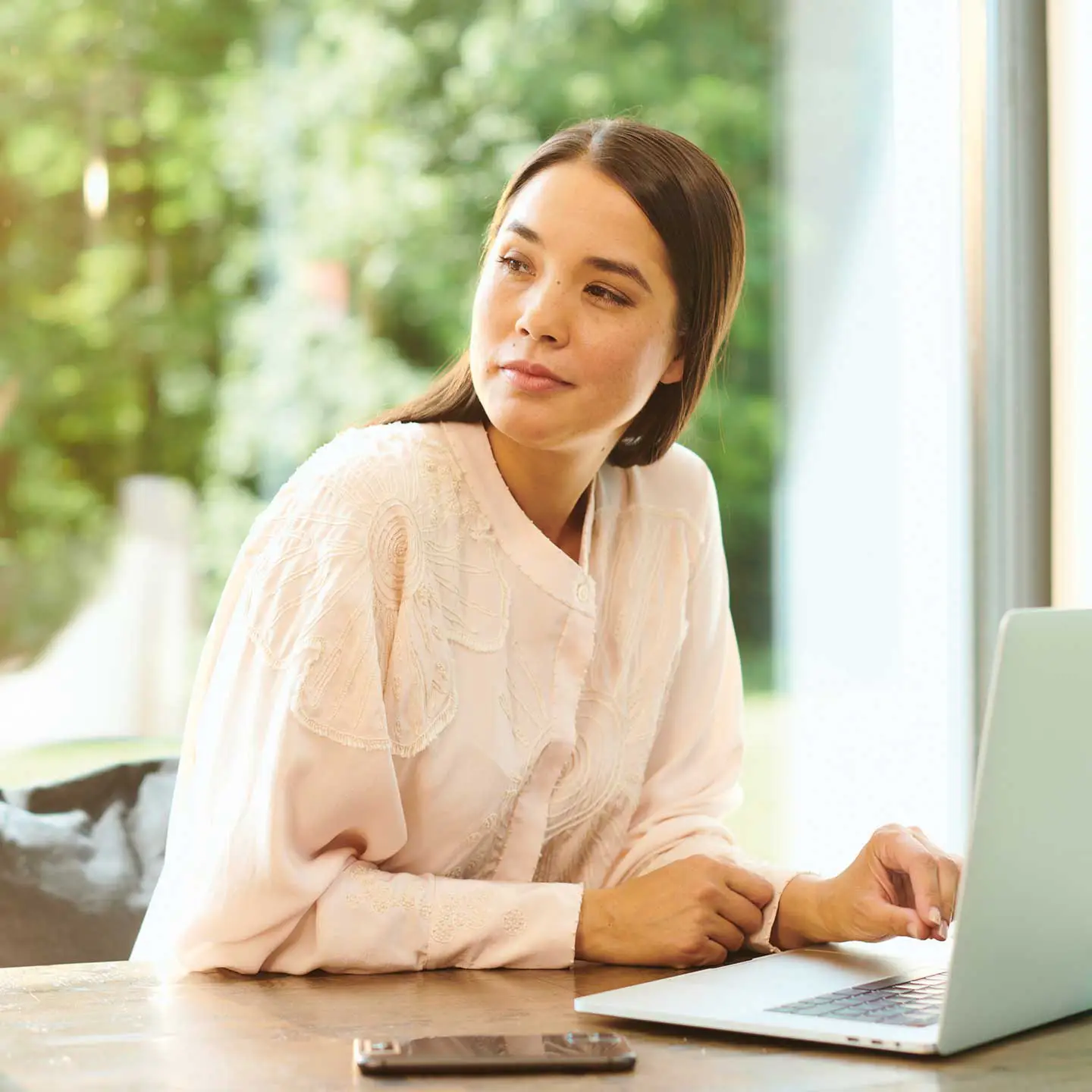 Frau mit skeptischem Blick und Smartphone und Tablet am Tisch