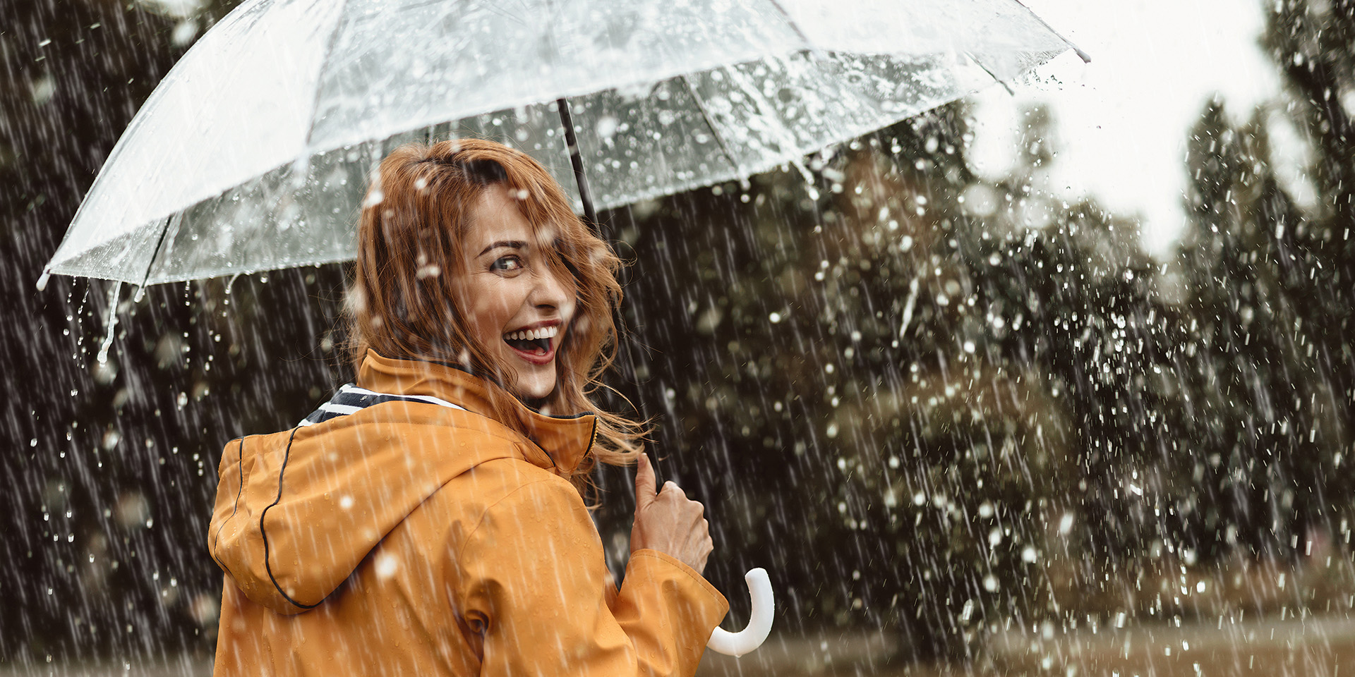 Frau steht im Regen unter dem Regenschirm und lächelt
