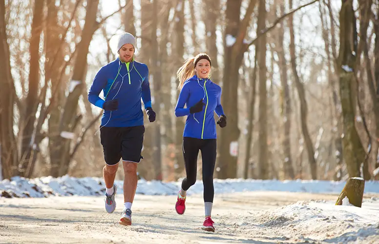 A female jogger and a male jogger in the snow-covered park