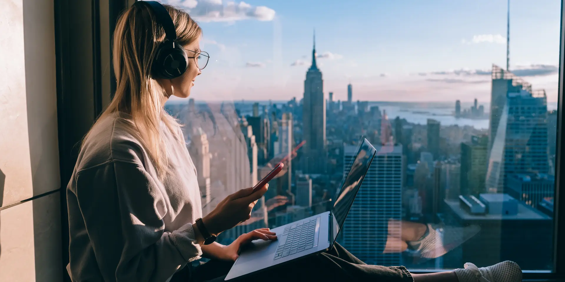New Work, Homeoffice, Remote Frau bei der Arbeit am Fenster mit Blick auf New York