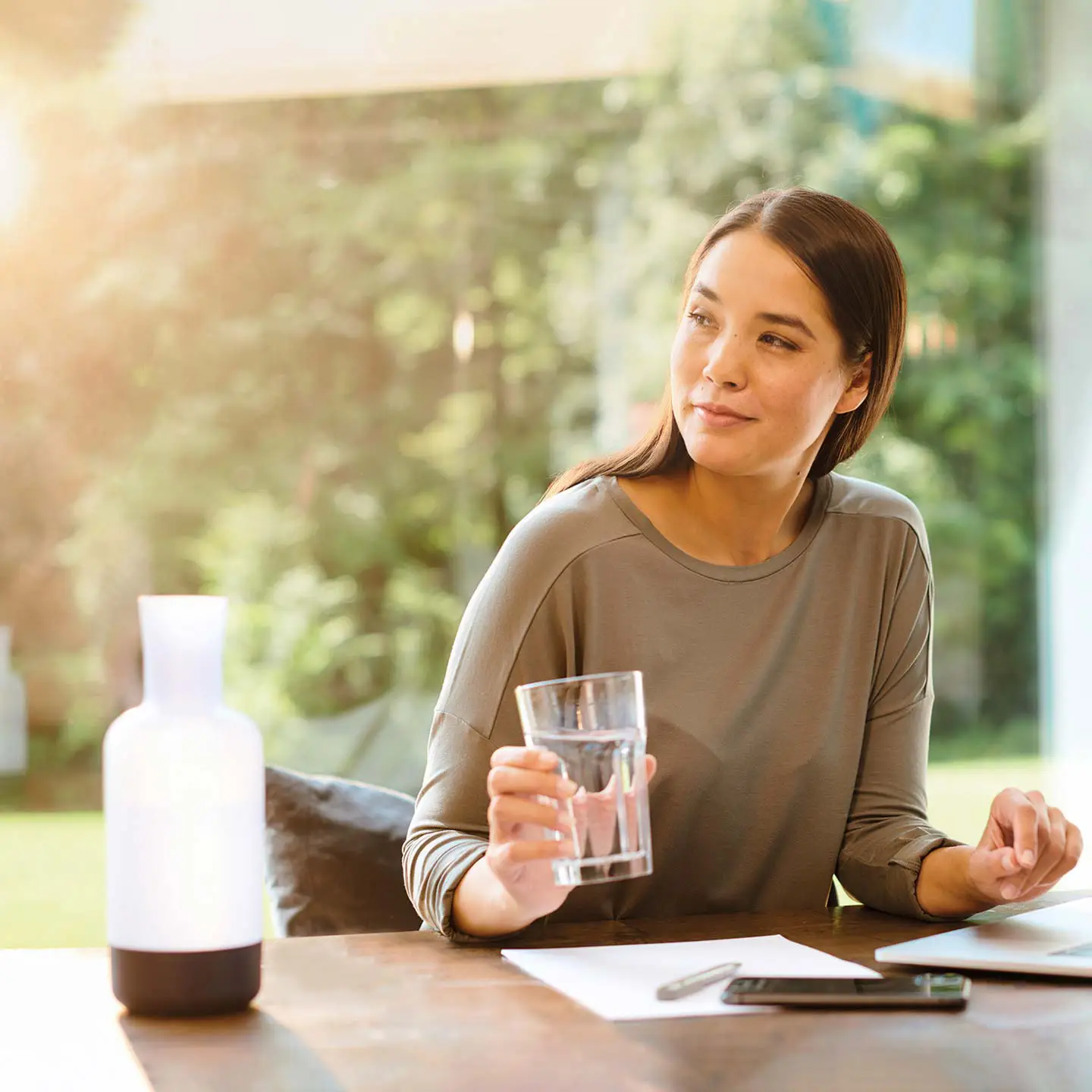 Une femme dans son bureau à domicile devant son ordinateur portable, un verre d'eau à la main