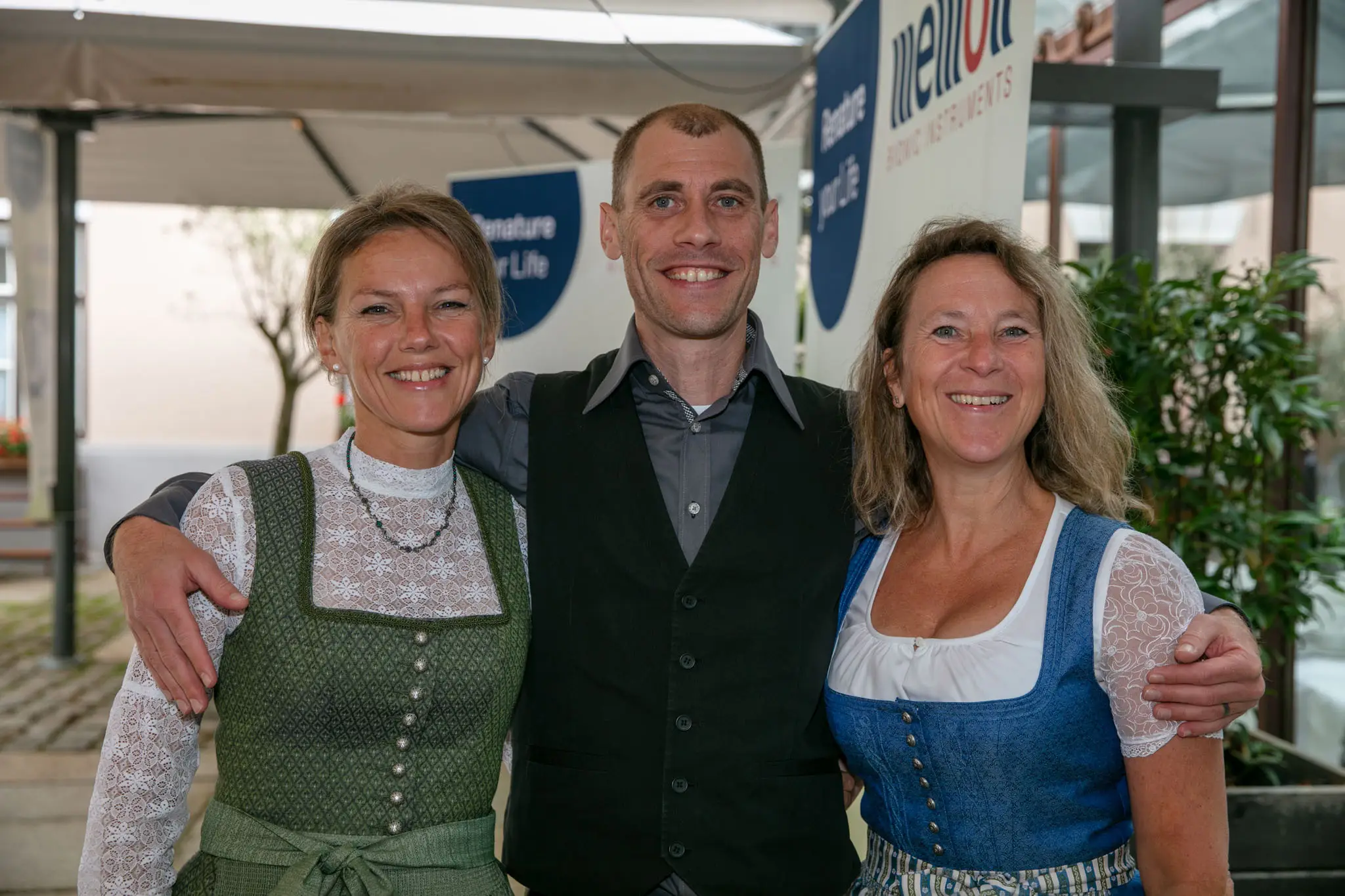 two women and a man in the middle dressed in traditional costume smile at the camera