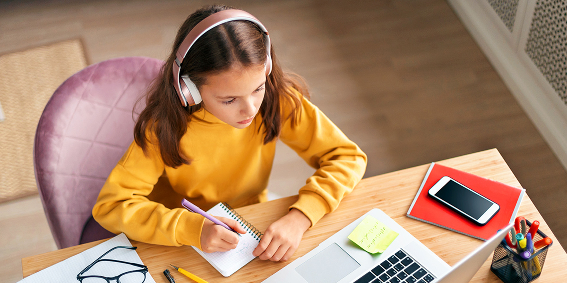 Kind sitzt am Schreibtisch, mit Laptop, Handy und Bluetooth-Kopfhörern