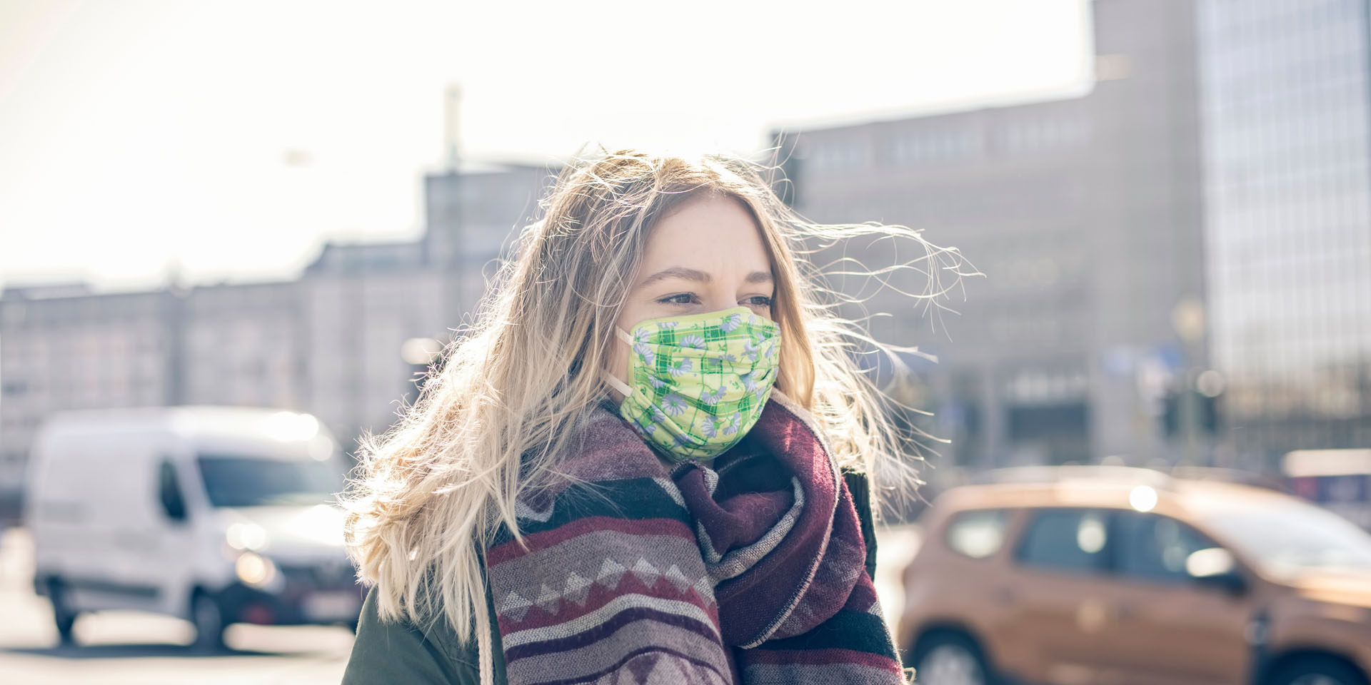 Junge Frau mit einer Maske an einer starke befahrenen Straße