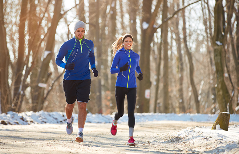 A jogger and a woman jogging in the park covered with snow