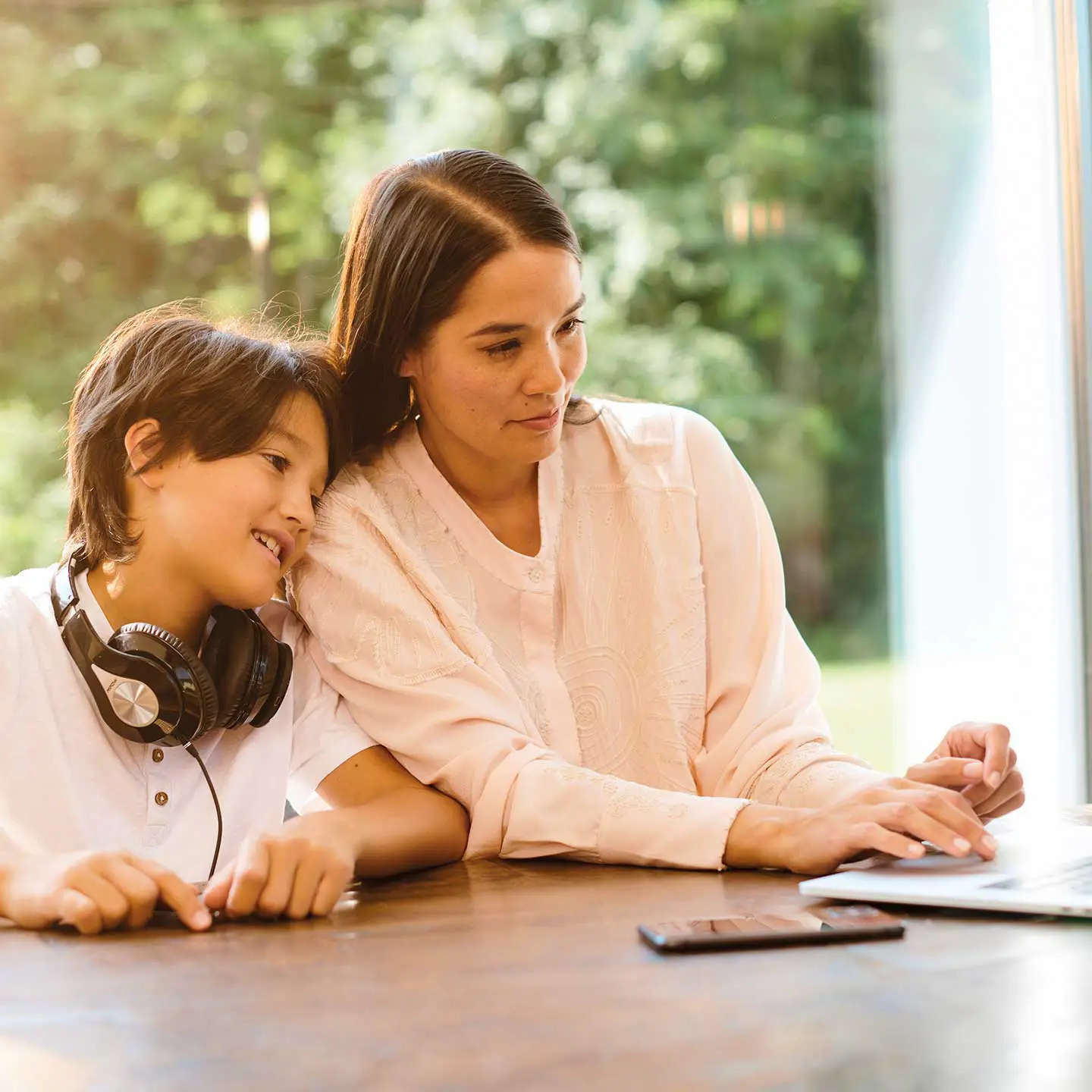 Une mère et son fils sont assis à table et regardent un ordinateur portable.