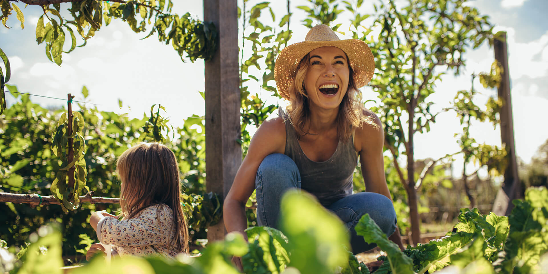 Mutter und Kind ernten Mutter und Tochter sitzen lachend zusammen im Gemüsegarten