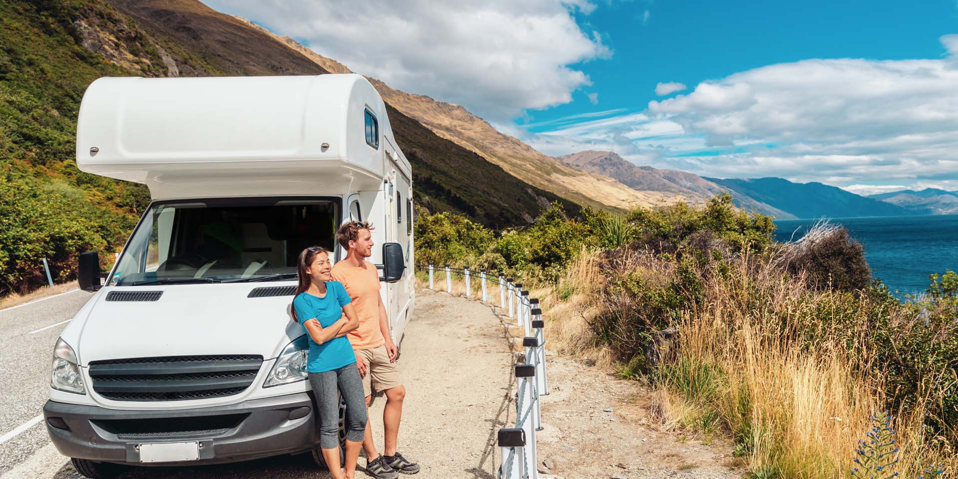 Young couple standing in front of their caravan looking out to sea