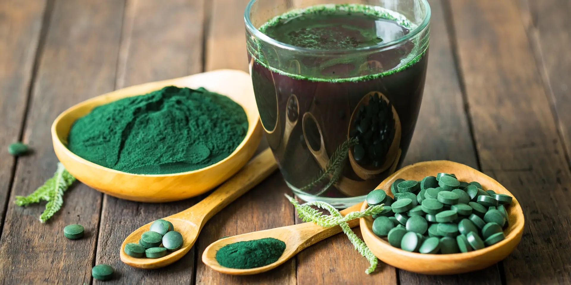 Spirulina mit höchster Qualität Spirulina in Form von Pulver, Tabletten und als Smoothie auf einem Holztisch