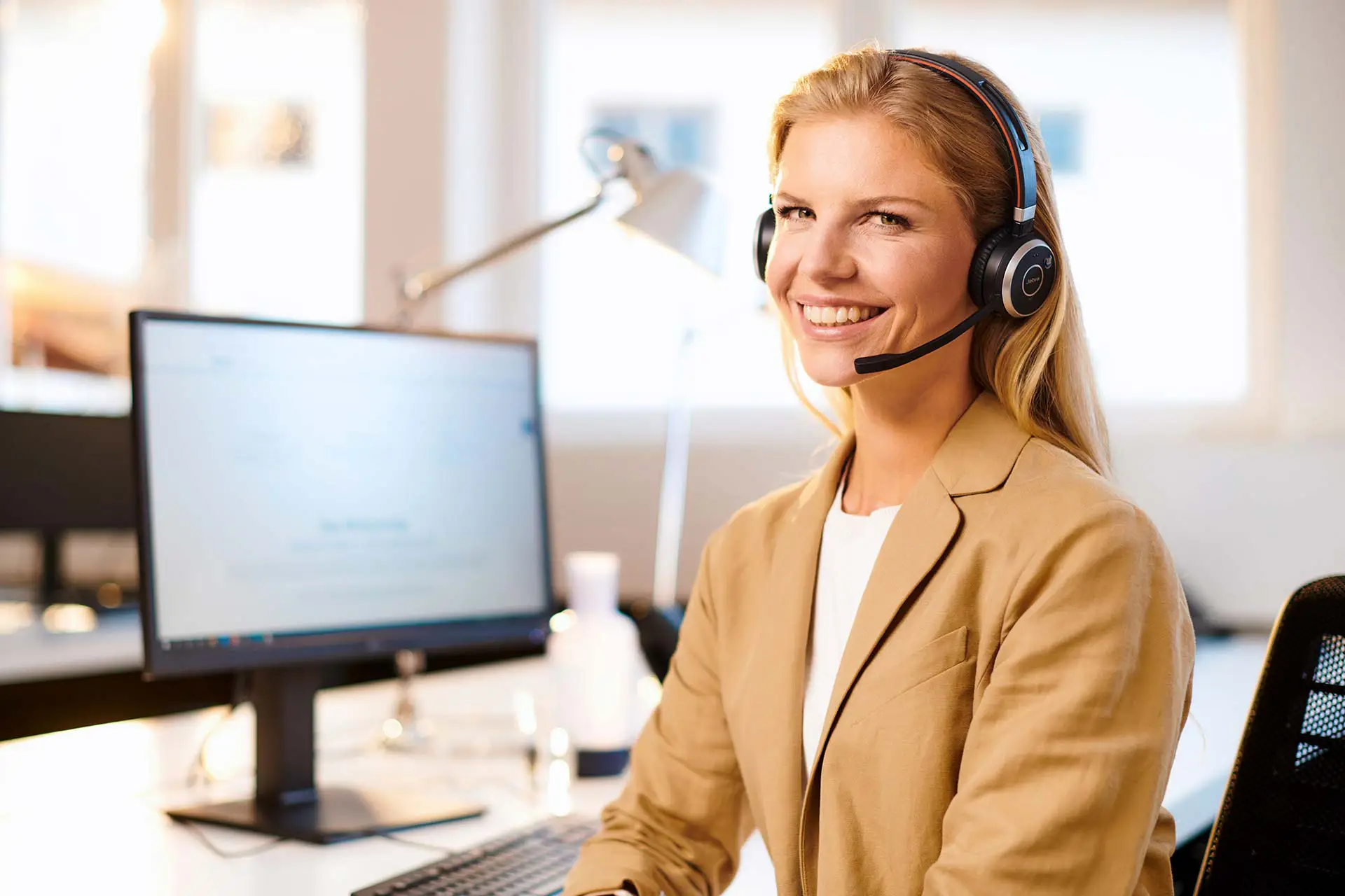 Frau am Schreibtisch mit Headset telefonierend