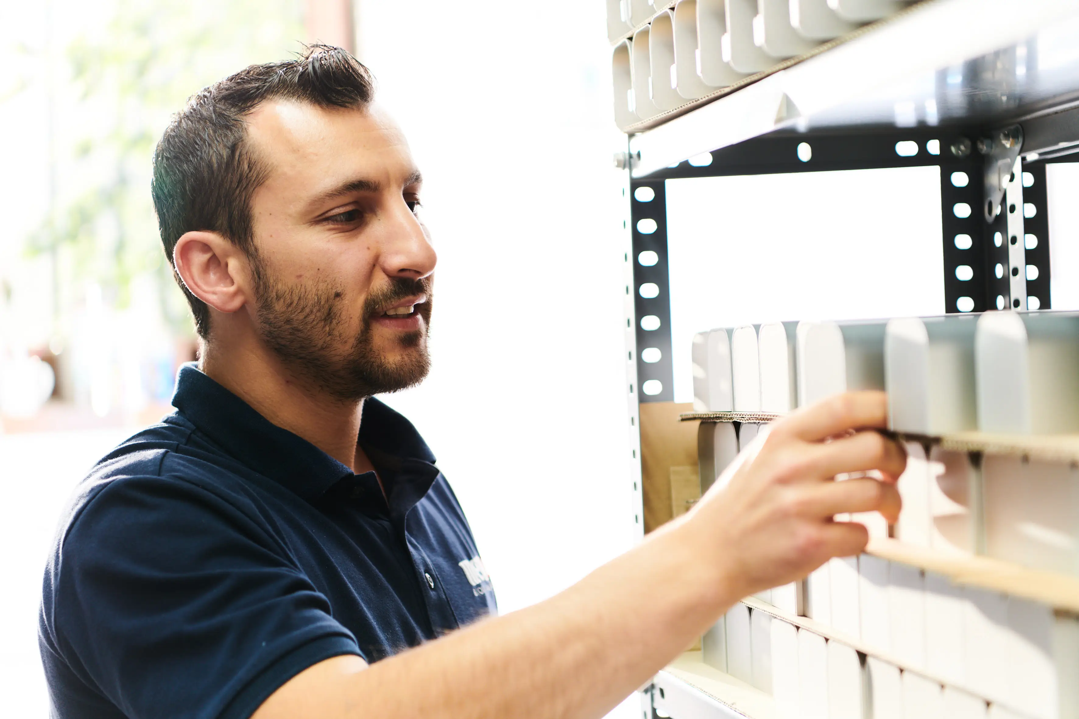 Stellenangebot - Produktion Ein Mann in einem blauen T-Shirt räumt ein Regal ein